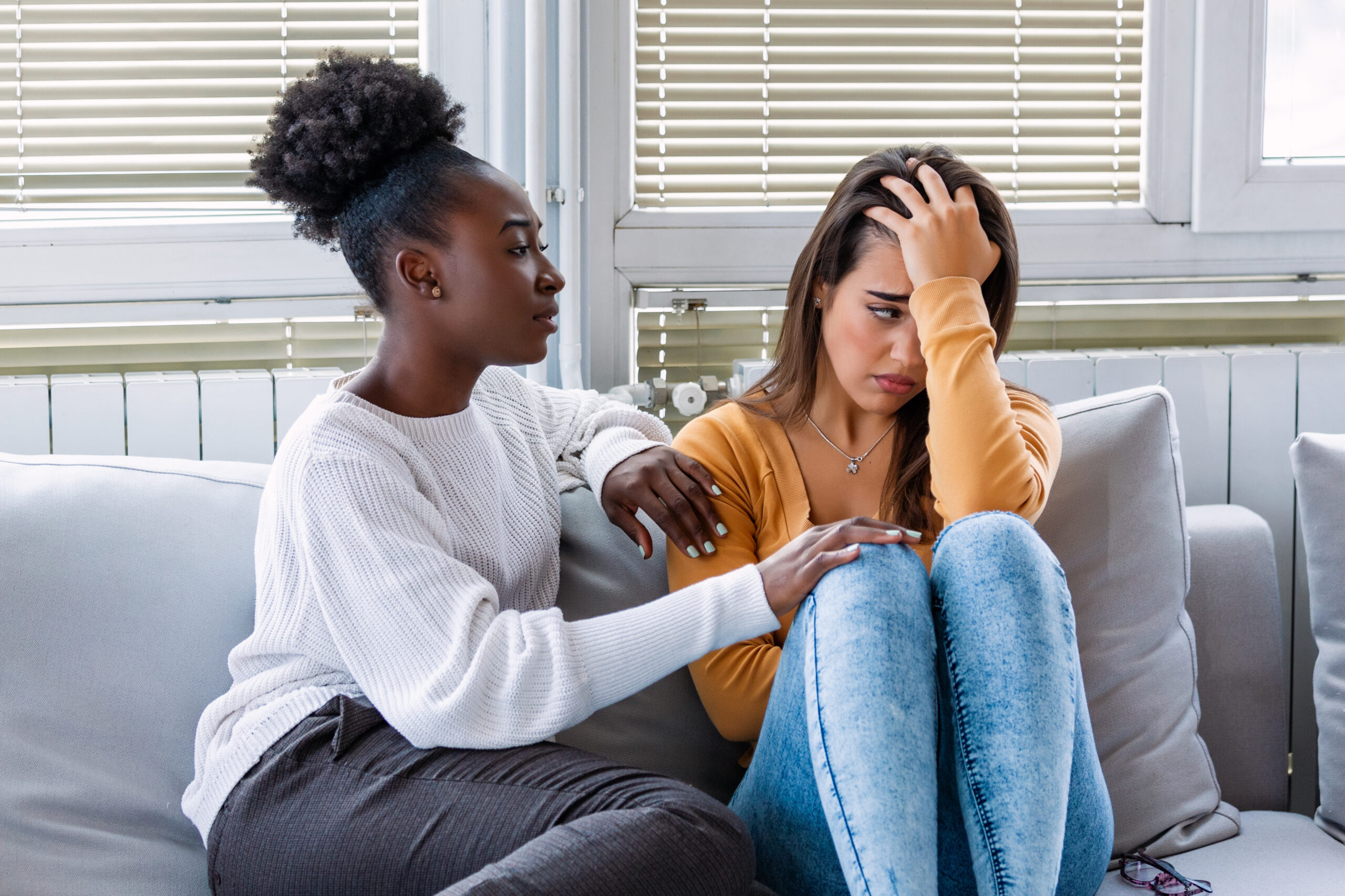 Woman hugging her depressed friend at home, closeup. Young girl supporting her crying girlfriend. Friendship consoling and care, copy space